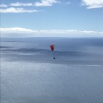 roter Gleitschirm fliegt über das Meer
